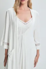 Bata de estar por casa color blanco, confeccionada en tejido suave con caída fluida. Presenta mangas tres cuartos con detalles de transparencias en los puños y el ruedo, bolsillos laterales y un lazo ajustable en la cintura.