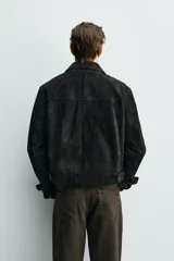 Cazadora de corte cropped confeccionada en piel con acabado de ante. Presenta cuello solapa, cierre frontal de botones, mangas largas con puños abotonados y bolsillos de plastrón con solapa en el pecho. Incluye detalle de cinta trenzada en el bajo.