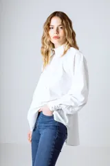Blusa blanca de algodón con cuello alto con volantes y botonadura frontal parcial. De manga larga con puños abullonados.