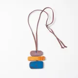 Collar largo con cordón de gamuza marrón ajustable, compuesto por tres piezas rectangulares de resina con efecto marmolado en tonos violeta, naranja y azul.