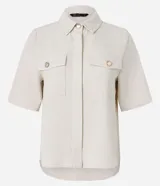 Camisa color fucsia de tejido airflow, con cuello camisero, mangas cortas con pliegues, cierre frontal con botones metalizados y bolsillos con solapa en el pecho.