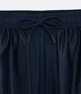 Bermuda deportiva gris con cintura elástica, cordón de ajuste, bolsillos con cremallera, recorte lateral con agujeritos y abertura en el bajo.