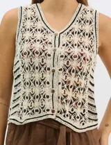Chaleco de tejido crochet con diseño calado de motivos florales y geométricos. Presenta escote en V, cierre frontal con botones y detalles de vivos a contraste en color negro en sisas, escote y ruedo.
