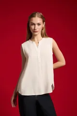Blusa evasé de viscosa color blanco, sin mangas, con cuello a la base y escote en V con cartera frontal.