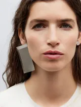 Par de aros asimétricos plateados. Uno es un botón pequeño y el otro es un prisma rectangular.