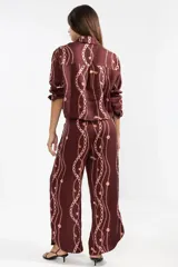 Pantalón de lino italiano color borgoña con estampado de cadenas en color rosa. De corte recto y talle medio, con cintura elástica en la parte posterior, bolsillos delanteros y aberturas laterales en el ruedo.