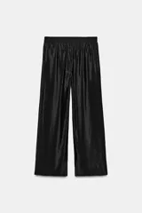 Pantalón de tiro alto color verde militar, confeccionado en tejido satinado con acabado brillante. Presenta cintura elástica fruncida, bolsillos laterales ocultos en las costuras y perneras de corte ancho.