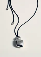 Collar largo con cordón negro ajustable y dije metálico de diseño orgánico y minimalista.