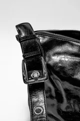 Bandolera negra de cuero sintético con acabado brillante y arrugado. Tiene una correa ajustable y un cierre de cremallera en la parte superior.