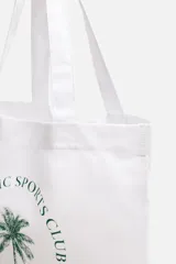 Bolso tipo shopper blanco de tela con asas de hombro. Estampado frontal con texto "Athletic Sports Club", una palmera y la frase "Embrace the lifestyle" con el año "Est. 1975".
