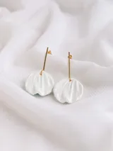 Aros colgantes con perno dorado y un dije de porcelana blanca en forma de pétalo o concha marina.