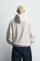Sudadera tipo hoodie de color blanco hueso, con capucha, manga larga y bolsillo canguro frontal. Presenta un calce relajado y tejido de algodón con interior afelpado.