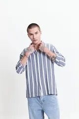 Camisa de manga larga con textura rústica y diseño de rayas verticales en tonos azul y blanco. Presenta un corte regular, cuello clásico y cierre frontal con botones.