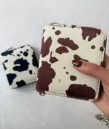 Billetera cuadrada con cierre de cremallera y estampado de vaca en blanco y negro o blanco y marrón.