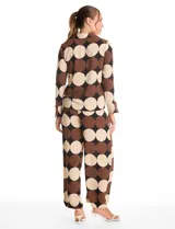 Conjunto de dos piezas compuesto por camisa de manga larga con nudo frontal y pantalón estilo palazzo de pierna ancha. Ambas prendas presentan un estampado geométrico de círculos grandes en tonos marrón, negro y beige. La camisa cuenta con cuello solapa y cierre frontal con botones, mientras que el pantalón posee tiro alto y corte holgado.