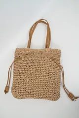 Bolso tipo tote de tejido estilo rafia en color beige, con asas dobles de hombro y cordones ajustables de cuero sintético marrón.