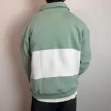 Buzo de algodón con medio cierre frontal y cuello tipo polo. Presenta un diseño de bloques de color en tonos gris oscuro y blanco, con bordados decorativos en el pecho.