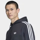 Canguro con capucha Adidas color negro, con las clásicas tres tiras blancas en las mangas y el logo del Trifolio bordado en el pecho. Cuenta con bolsillo tipo canguro y cordón ajustable en la capucha.