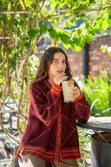 Saco tejido de punto con diseño de rombos en tonos bordó y naranja, con detalles de hilo lurex. Presenta cuello redondo, cierre frontal con botones, mangas largas abullonadas y terminaciones acanaladas en puños y ruedo.