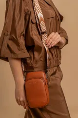 Bandolera compacta color rojo con textura de cuero, correa regulable y desmontable con diseño de rayas rojas y blancas. Cuenta con bolsillos frontales y cierre, interior forrado en tela.