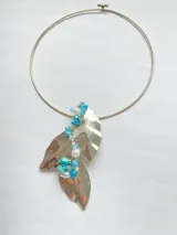 Gargantilla rígida plateada con dije colgante de dos hojas de alpaca con detalle de piedras turquesas y perlas.