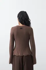 Top de tejido acanalado con sutil acabado metalizado, de silueta entallada con diseño peplum en la cintura y mangas largas levemente acampanadas.