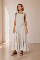 Vestido largo sin mangas de lino en color beige, de corte evasé y diseño holgado, con costuras decorativas diagonales en contraste de tono oscuro en la parte frontal y ribetes oscuros en el cuello y las sisas.