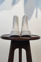 Bota tipo Chelsea de caña corta en color beige, confeccionada en material sintético con acabado liso. Presenta paneles elásticos laterales a tono y una suela track robusta y dentada que aporta altura y estilo moderno.
