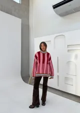 Buzo oversize de punto con cuello alto, mangas largas y diseño a rayas verticales en tonos rosa y bordó.