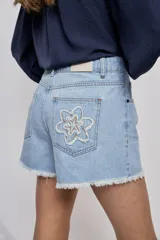 Short de denim blanco de calce recto y tiro medio, con bolsillos delanteros, cierre con botón y terminación desflecada en el ruedo. Presenta detalles florales bordados al tono en el frente.