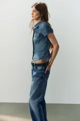 Camisa entallada de denim de manga corta, cuello camisero, bolsillos delanteros con solapa y cierre frontal de botones.