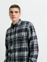 Camisa de franela de manga larga con estampado de cuadros escoceses. Presenta cuello button-down, cierre frontal con botones de madera y dos bolsillos tipo parche en el pecho con cierre de botón.