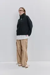 Pantalón cargo negro de corte relajado y pierna ancha con bolsillos laterales con solapa, cintura con doble broche y cierres metálicos en los tobillos.