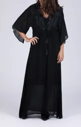 Vestido largo negro de crepé con escote en V, mangas 3/4 acampanadas y bordado floral en el canesú. Ajuste con lazo y borlas en la cintura.