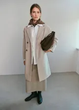 Abrigo midi de corte recto en color beige, con cuello de solapa con muesca y cierre frontal de doble botonadura. Cuenta con manga larga y dos bolsillos laterales con solapa.