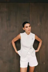Top de denim blanco sin mangas, con cuello mao y cierre frontal cruzado con trabillas y botones metálicos.