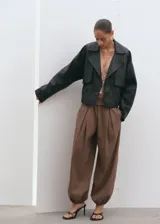 Pantalón balloon de tiro alto color marrón, confeccionado en algodón, con cintura ajustable con elástico, pinzas en la parte delantera, bolsillos laterales y bajos fruncidos con elástico.