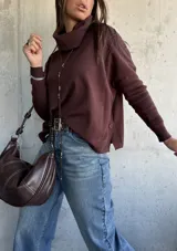 Sweater de tejido de punto color chocolate, con cuello polera, mangas largas con puños acanalados y diseño holgado con aberturas laterales y detalle de botones.