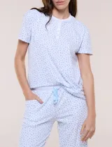 Pijama de dos piezas con estampado floral en tonos azules sobre fondo blanco, compuesto por una remera de manga corta con cuello redondo y botones frontales, y un pantalón capri con cintura elastizada y bolsillos.