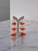 Caravanas colgantes con diseño de flores compuestas por pétalos de acrílico rojo y perlas centrales, unidas por una cadena dorada.