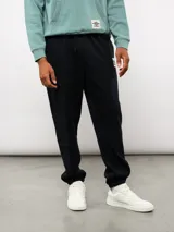 Pantalón jogger de felpa color negro, con cintura elástica, puños en los tobillos y etiqueta con el logo de la marca en la parte frontal.