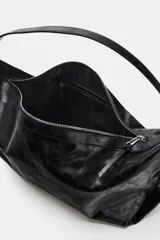 Bolso de hombro de diseño hobo en color negro, con acabado efecto cuero desgastado. Cuenta con asa ajustable, cierre principal mediante cremallera y detalles metálicos en los laterales.