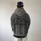 Canguro oversize gris con efecto lavado desgastado, capucha y gran aplique bordado en la espalda.