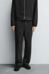 Pantalón regular fit color marrón oscuro, confeccionado en tejido con viscosa. Cuenta con cintura elástica, bolsillos delanteros y detalle de bolsillos traseros de vivo. El cierre frontal es con cremallera y botón.
