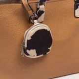 Cartera tipo tote de color marrón, con diseño texturizado, asas de mano con estampado de vaca y un monedero colgante redondo con el mismo estampado.