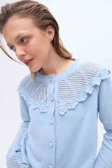 Saco color crudo confeccionado en tejido de punto, con cuello redondo y cierre frontal de botones. Presenta un canesú superior y puños acampanados con detalles de tejido calado y terminaciones de crochet.