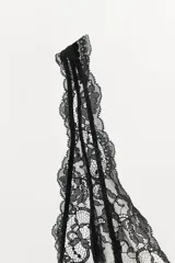 Body negro de corte cavado, con escote en V profundo y tirantes finos ajustables. La parte superior del busto es de encaje floral negro sobre una base clara, mientras que el cuerpo es de tela lisa y satinada.