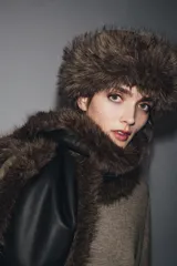 Gorro de estilo ruso con parte superior de cuero sintético negro y borde ancho de piel sintética en color marrón. Presenta costuras marcadas en la parte superior.