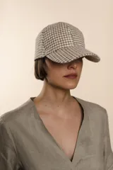 Gorra con visera confeccionada en lana fina sin teñir, con un sutil patrón de tejido en espiga.