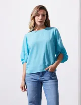 Blusa de gasa con estampado geométrico en tonos negro, gris y celeste. Tiene cuello redondo y mangas 3/4 amplias con abertura y botón.